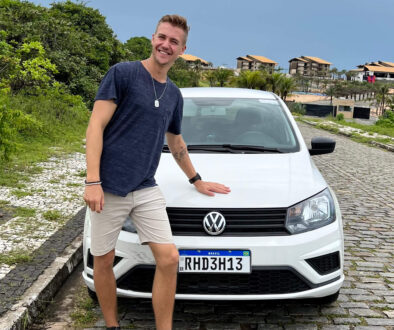 Max Haase is standing next to a white rental car with Brazilian license plates on a palm-lined coast.