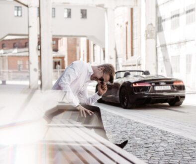 Max Haase laughing on a bench, behind him an Audi R8 Spyder in an industrial alleyway