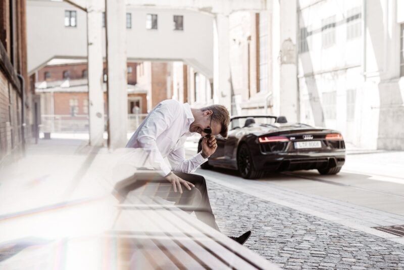 Max Haase laughing on a bench, behind him an Audi R8 Spyder in an industrial alleyway