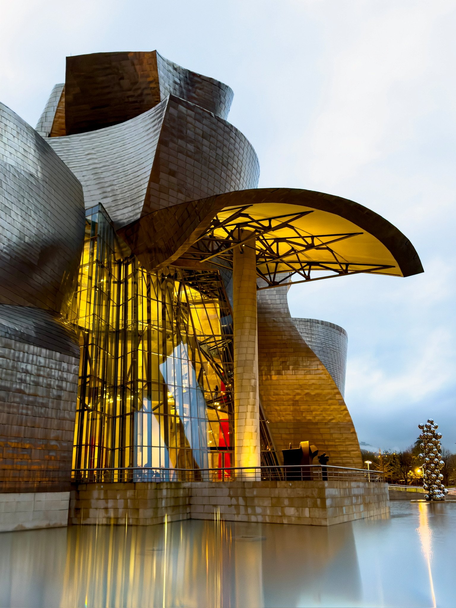 Eingangsbereich des Guggenheim-Museums Bilbao mit goldenem Vordach im Abendlicht