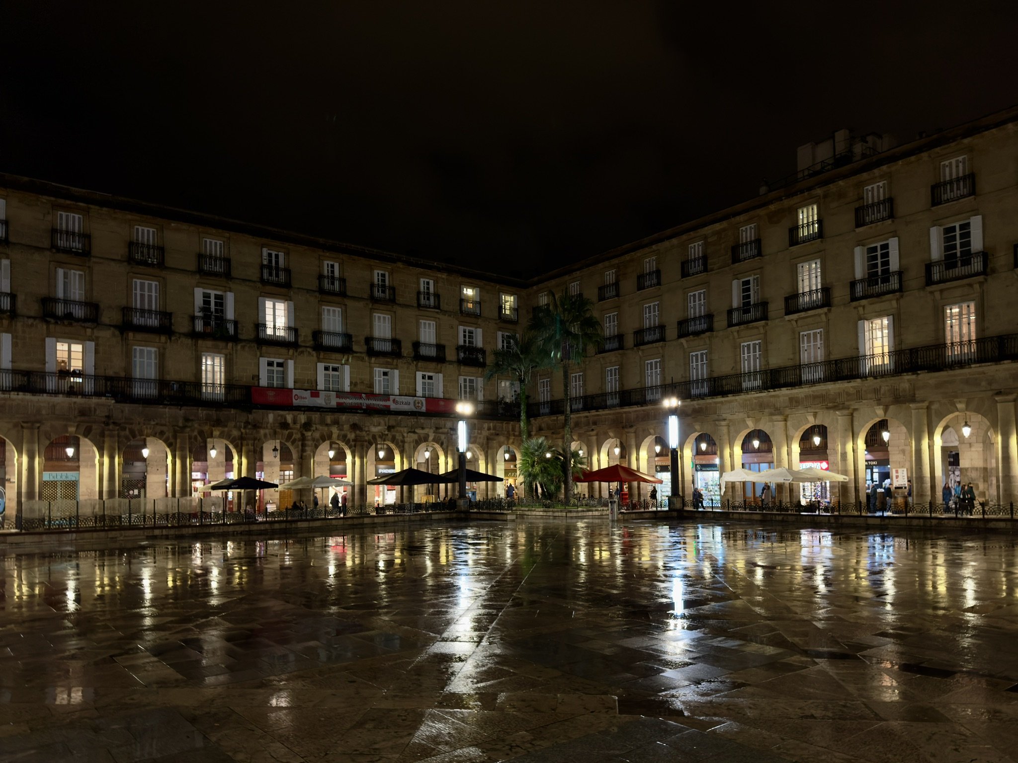 Plaza Nueva in der Altstadt von Bilbao bei Nacht mit Arkaden und nassem Pflaster
