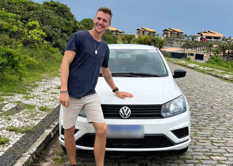 Max Haase is standing next to a white rental car on cobblestones