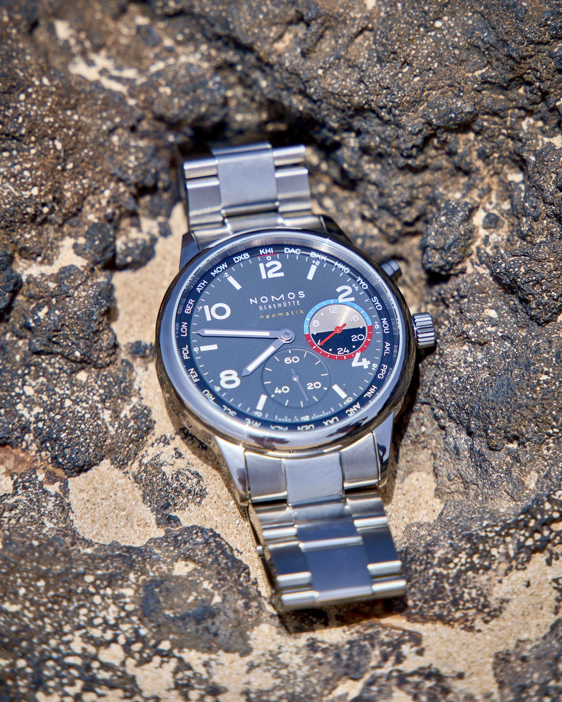NOMOS Glashütte wristwatch with steel bracelet on lava rock, product photo by Max Haase